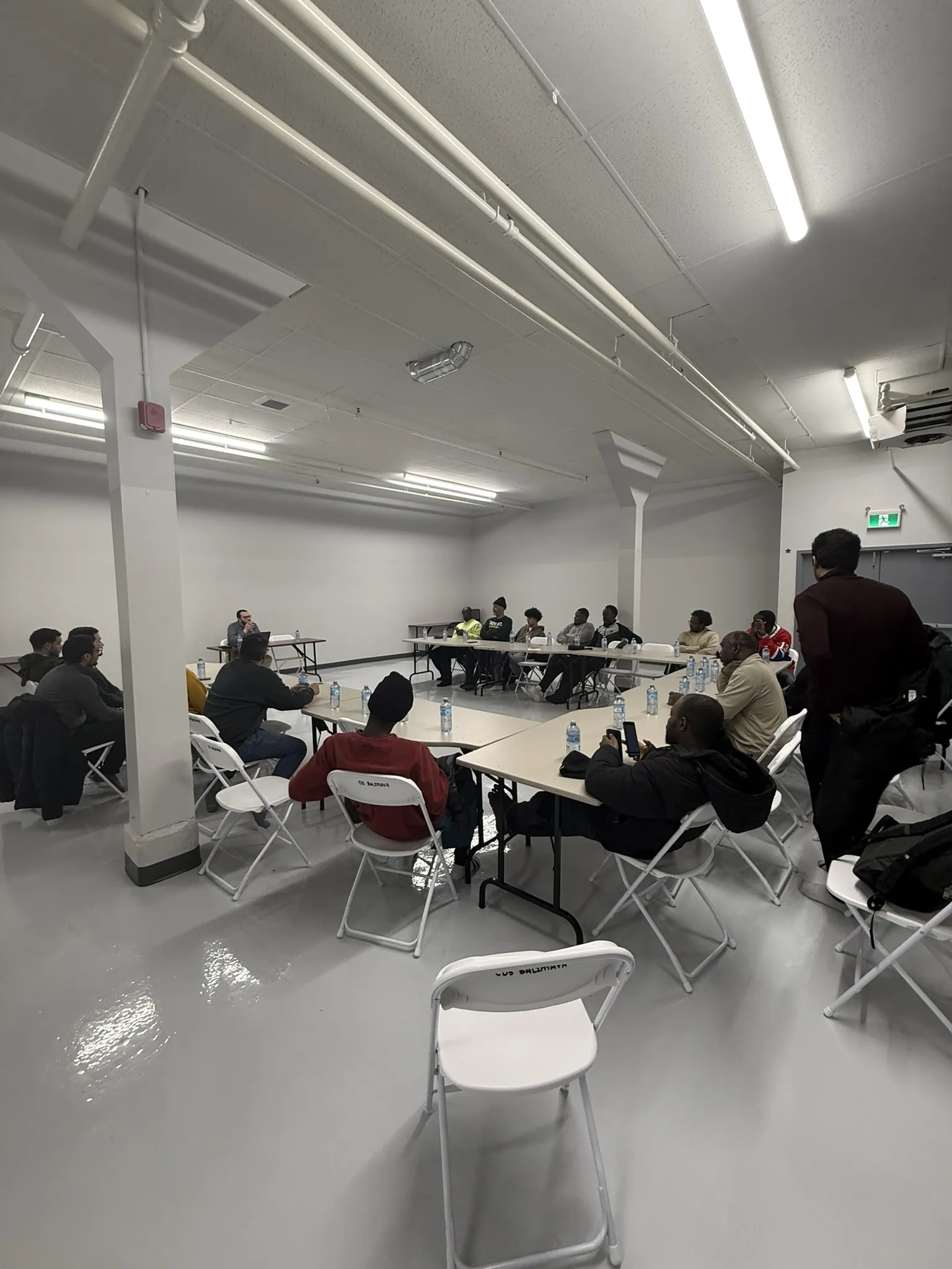La grande salle vide, tables et chaises le long des murs.