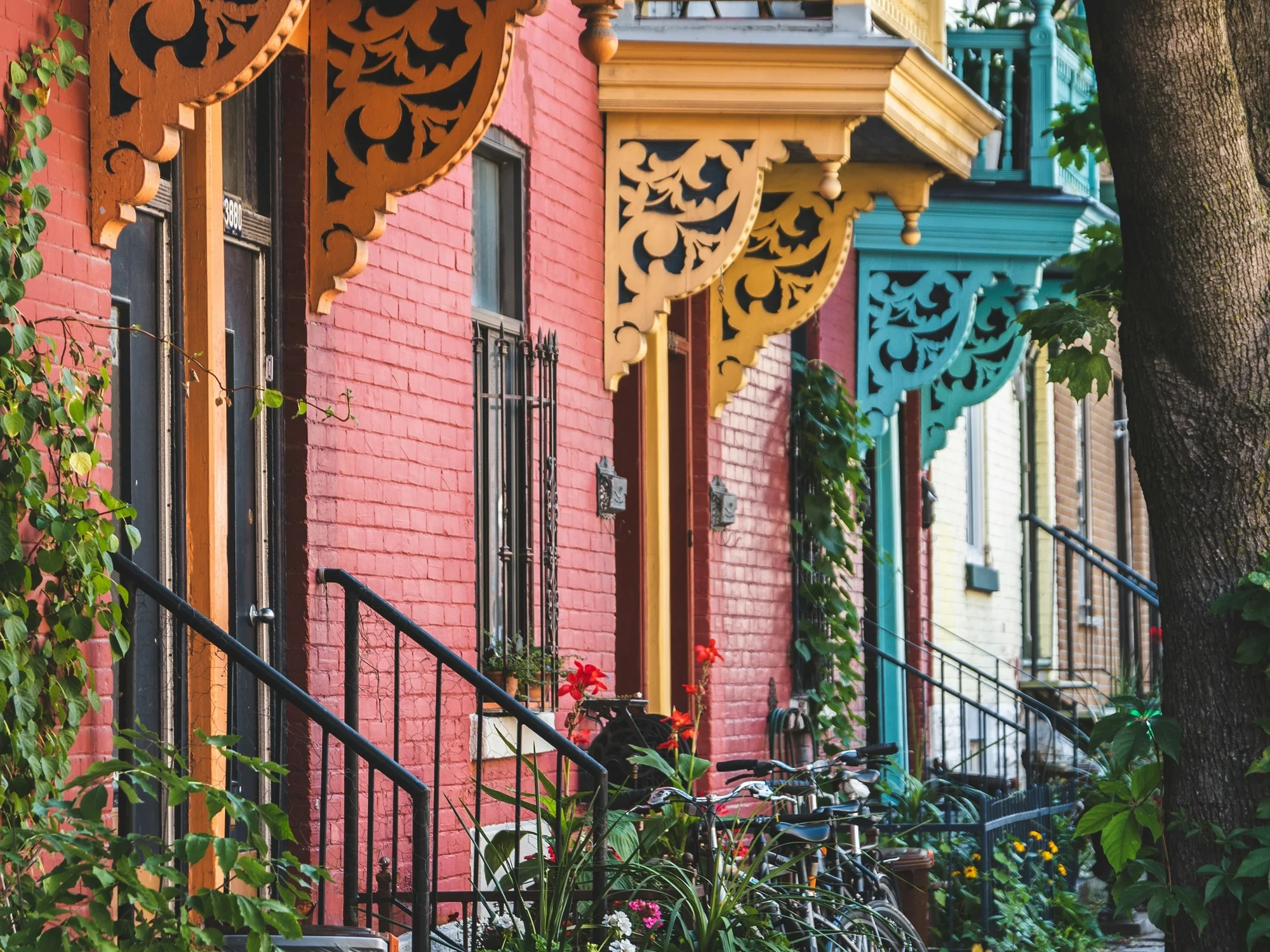 Une rue montréalaise en été : façades de briques colorées, corniches de bois ouvragé, escaliers et vélos.